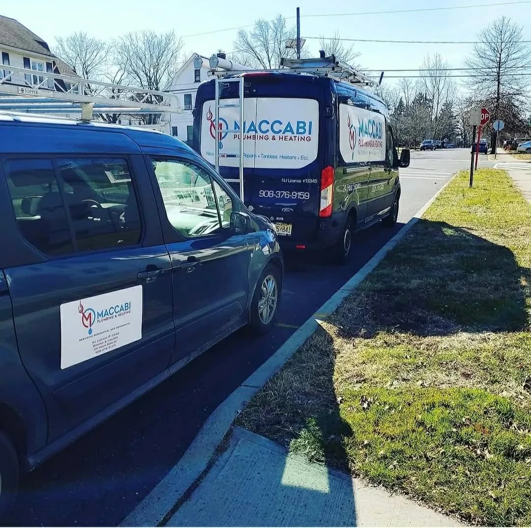 A Maccabi Plumbing & Heating service van and branded company car parked curbside on a residential northern New Jersey street