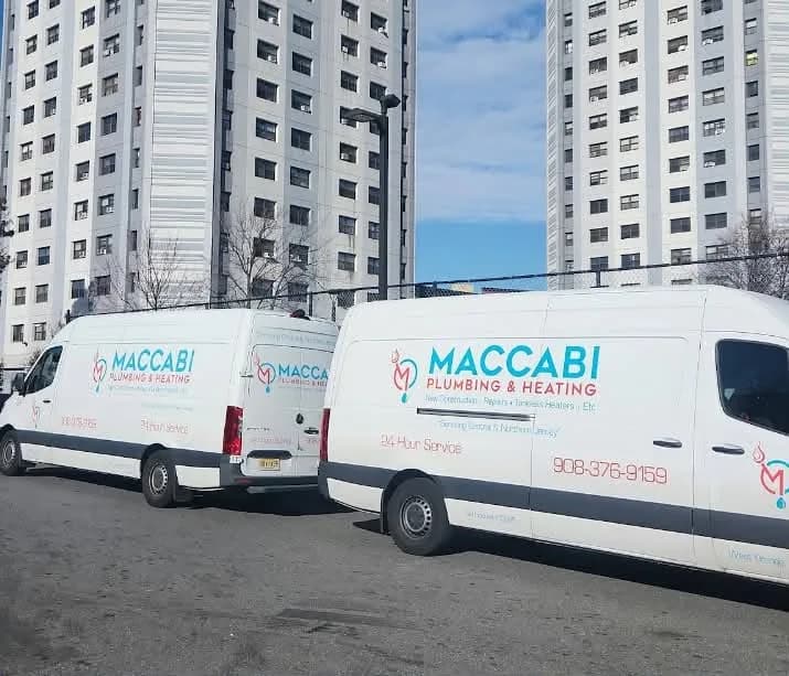 Two Maccabi Plumbing & Heating branded service vans parked outside a northern New Jersey apartment building