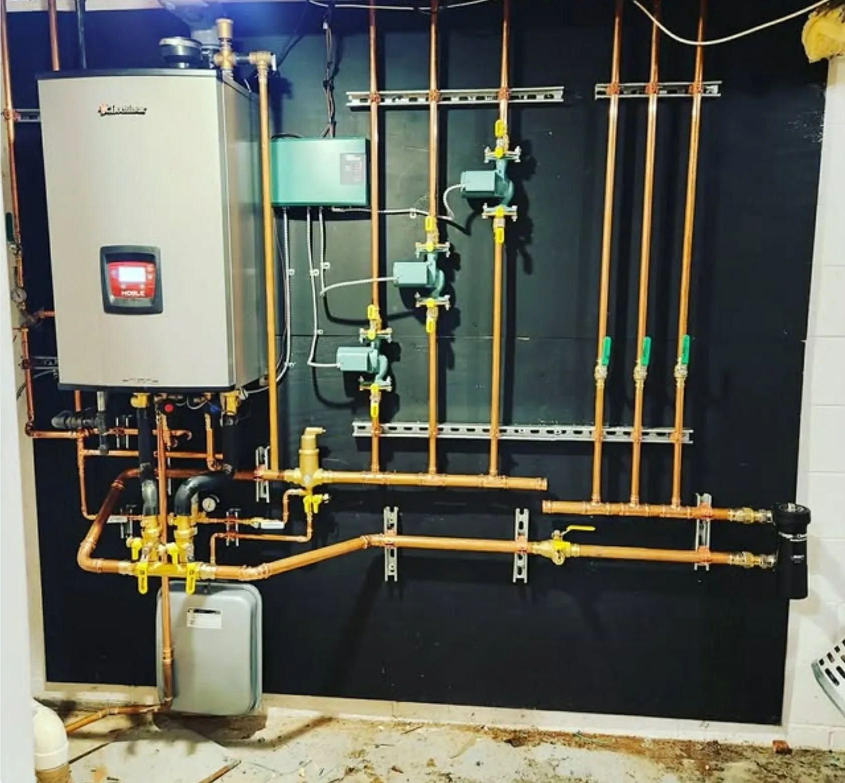 A wall-hung boiler with a copper zone manifold, circulator pumps and yellow gas piping in a northern New Jersey basement