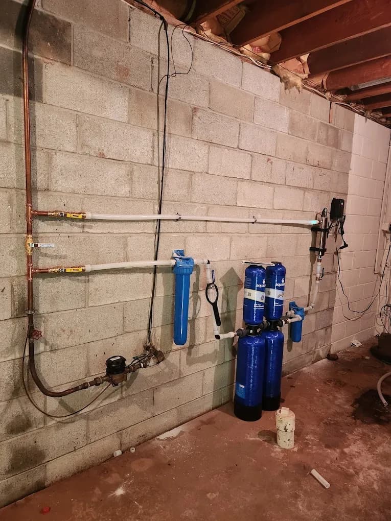 Copper and PEX water lines running along a basement block wall beside whole-house filter tanks after a repipe