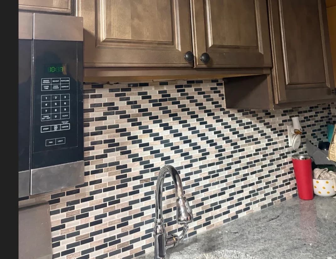A pull-down kitchen sink faucet against a mosaic tile backsplash after installation