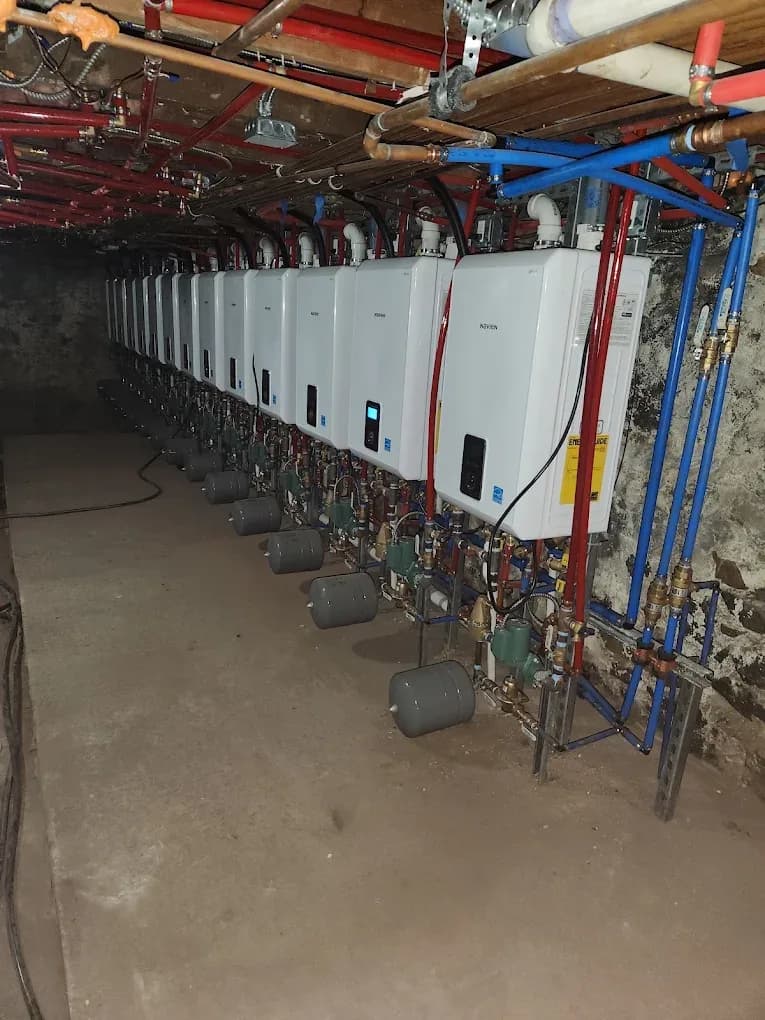 A bank of wall-mounted tankless water heaters with red and blue manifold piping in a northern New Jersey mechanical room