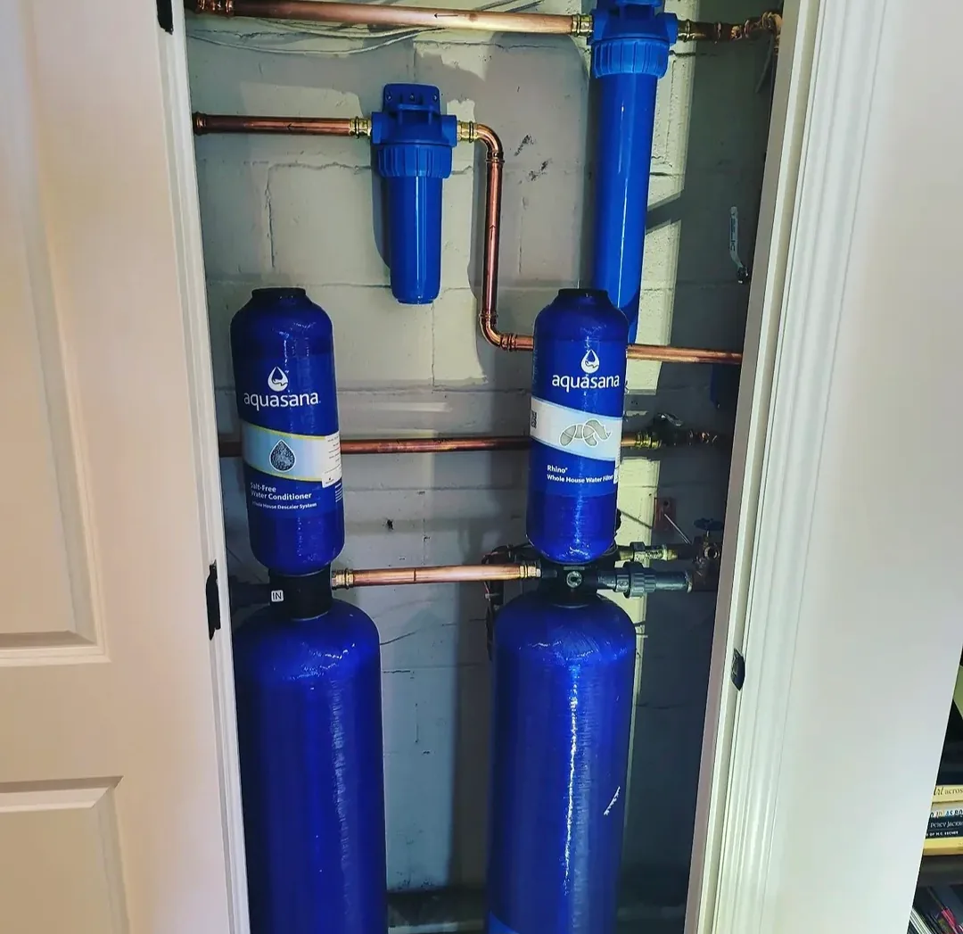 Two Aquasana whole-house water filtration tanks with blue pre-filters and a copper manifold