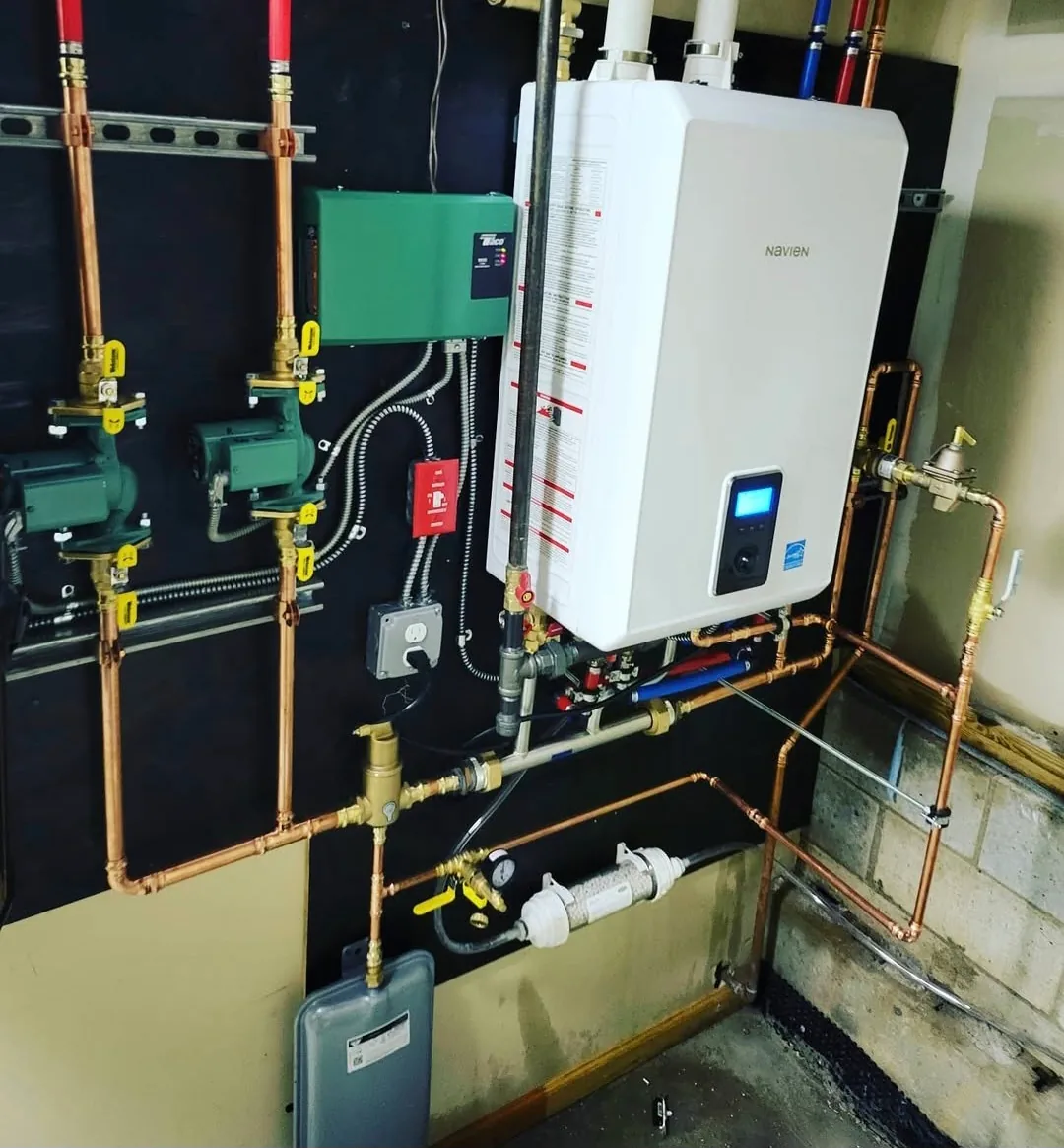 A wall-mounted condensing combi boiler with copper primaries, green-handled zone valves and gas piping